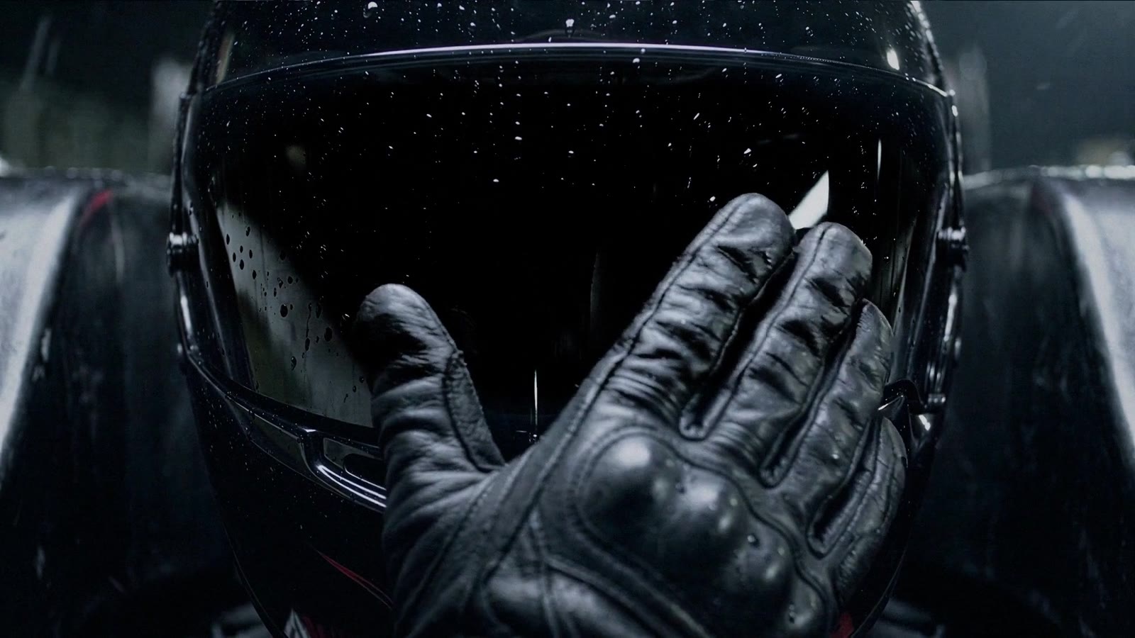 A gloved hand wiping a rain-covered visor
